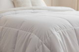 White comforter on a bed in a bedroom setting with plants and a side table.