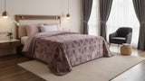 Modern bedroom with a bed covered in a patterned pink blanket, nightstands, and a chair.