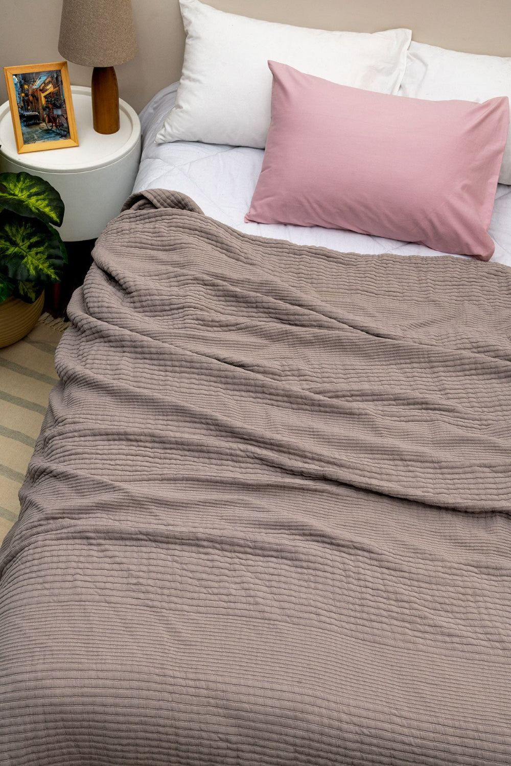 Elenor Coverlet  and pink pillow, nightstand with lamp and plant in the background