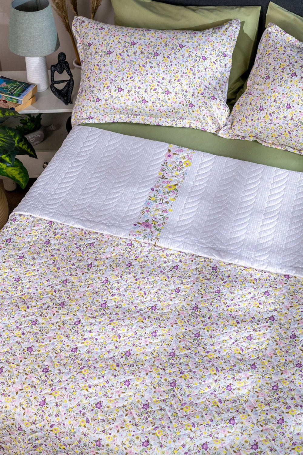Floral bedding set on a bed with a lamp and books in the background.