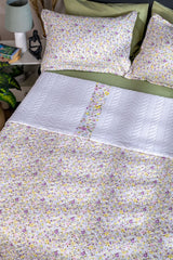 Floral bedding set on a bed with a lamp and books in the background.