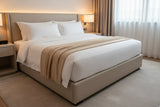 Neatly made bed with beige and white bedding in a bedroom setting.