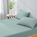 Teal bed sheets and pillows on a bed with a side table and plant in the background.