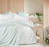 Bedroom with floral bedding and a side table with books and a plant.