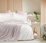 Bedroom with floral bedding and a side table with books and a plant.