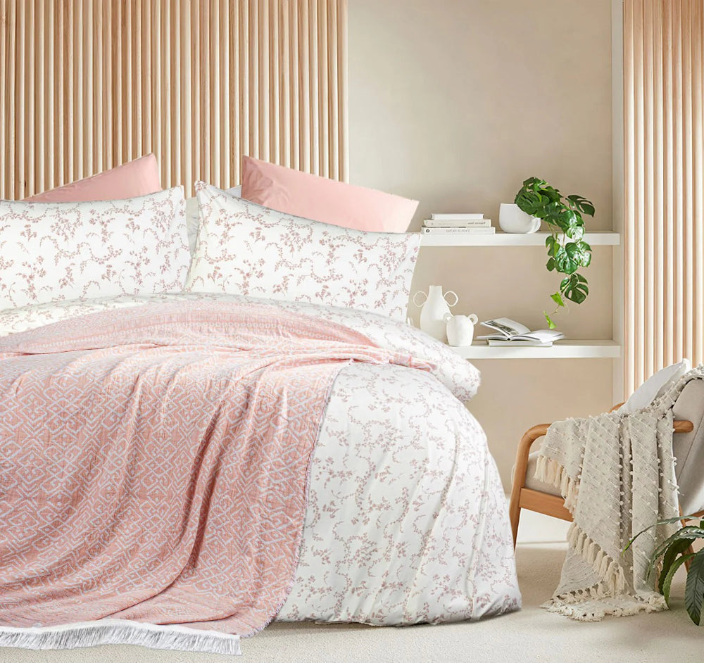 Bedroom with pink and white floral bedding and a side table with books and a plant.