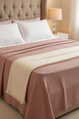 Bed with pink and beige checkered blanket, white pillows, and a lamp on a nightstand.